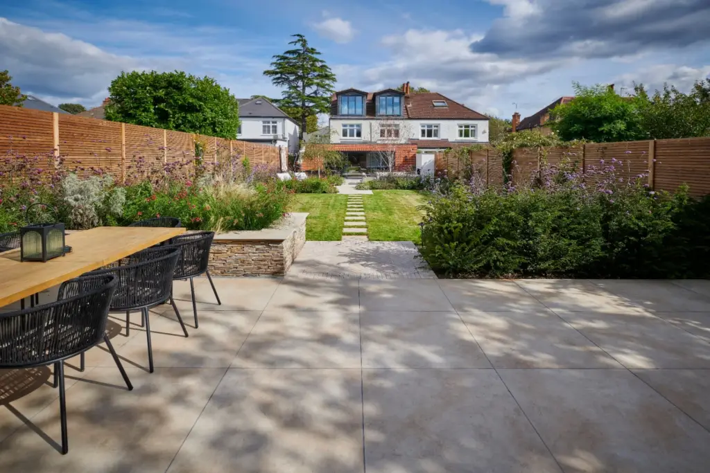 The Fire Terrace garden viewed from the lower lawn towards the house, with herringbone paving and lush planting framing the route.
