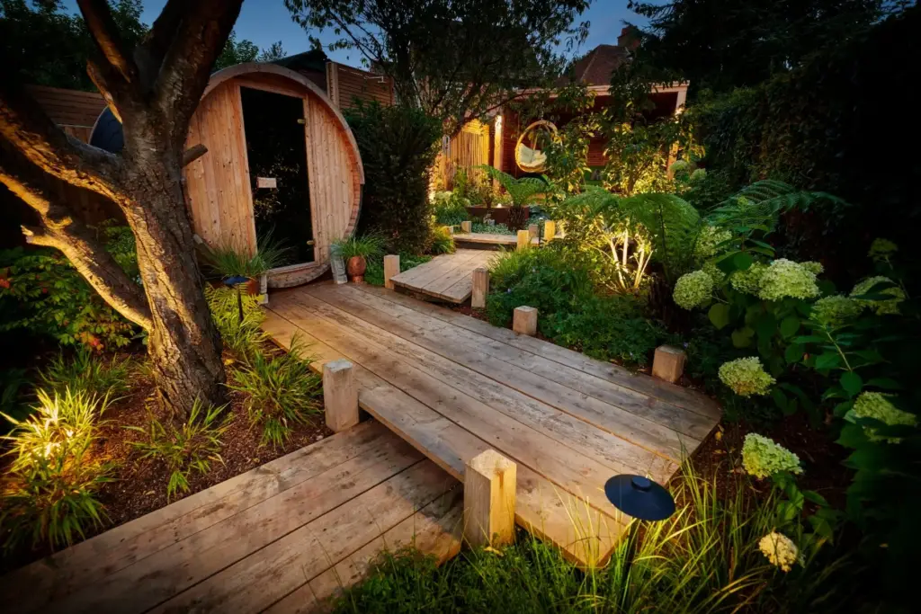 Barrel sauna with timber decking pathway at dusk with garden lighting