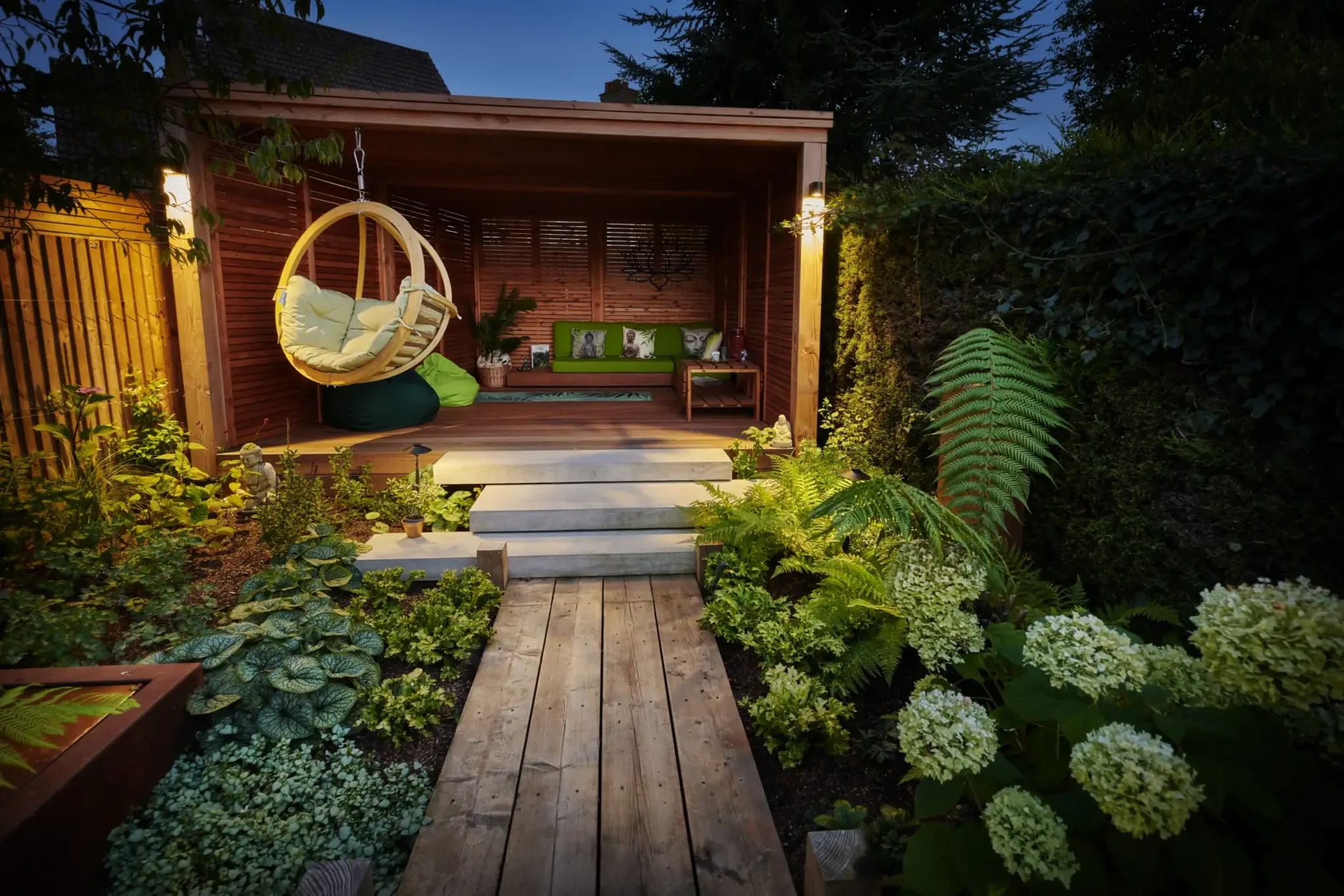 Jacob Berry’s wellness garden at dusk: the timber cabana with its hanging chair, the boardwalk and layered planting, designed and built by Refined Landscapes