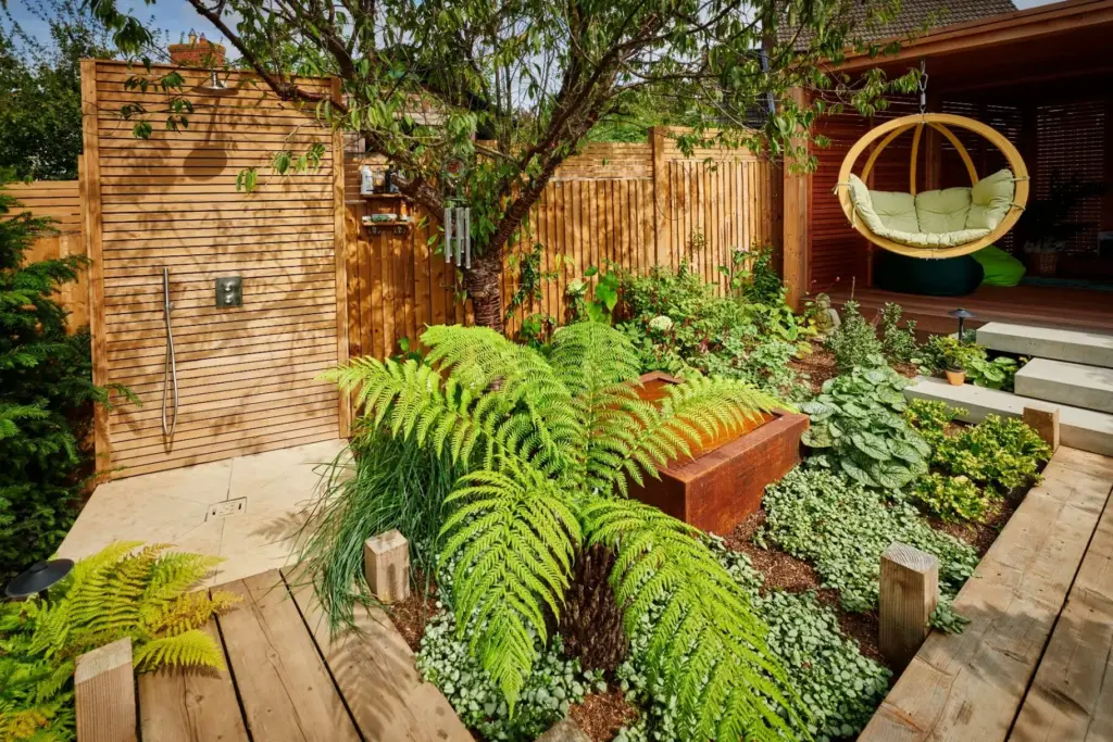 Outdoor shower area with cedar fencing, ferns and hanging swing seat