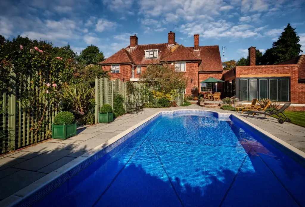Blue swimming pool with brick manor house and mature cottage garden