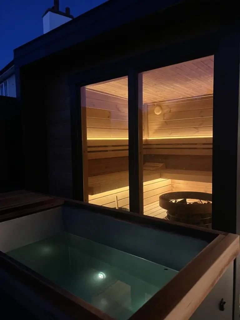 Illuminated sauna cabin with cold plunge tub at twilight
