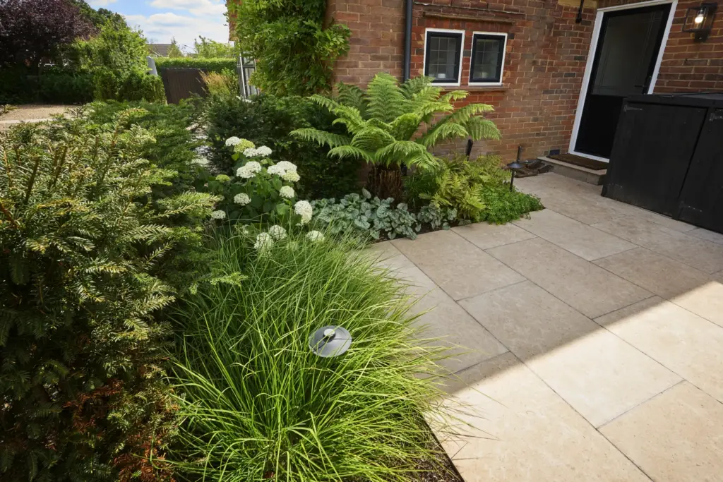 Paved garden seating terrace with contemporary outdoor furniture, framed by hydrangeas, ornamental grasses and clipped evergreen planting.