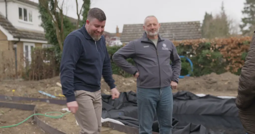 Two members of the Refined Landscapes team laughing on site beside a newly lined pond