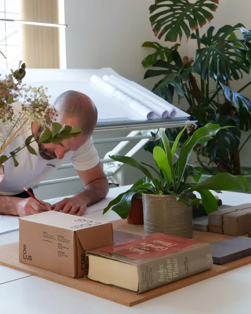 A Refined Landscapes designer drawing at the studio desk, surrounded by house plants and reference books
