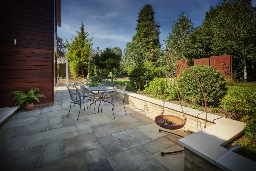 Dining terrace on Harvest sawn London Stone with a Corten fire bowl and steel screens beyond