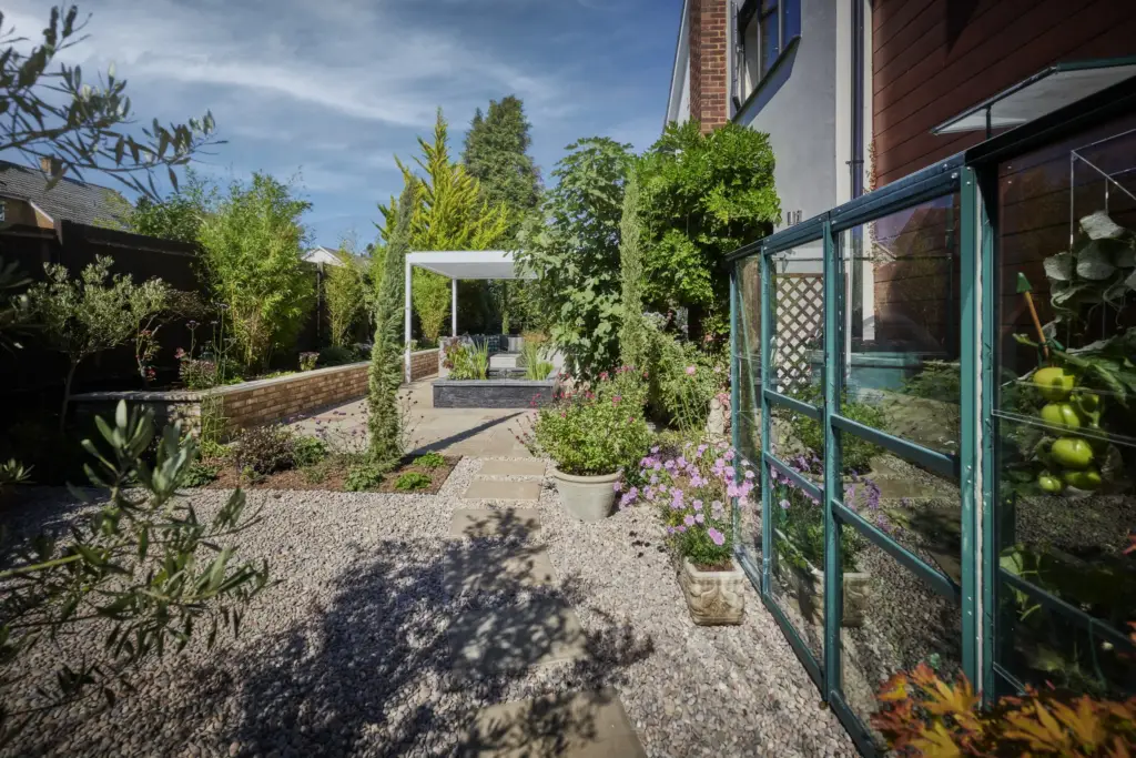 Gravel path through the productive garden with a greenhouse and cottage planting