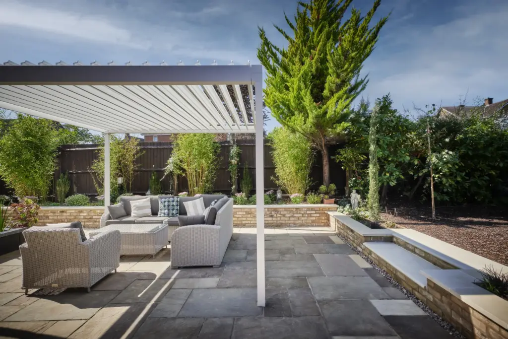 Louvred pergola over a seating terrace with pale paving and brick walls