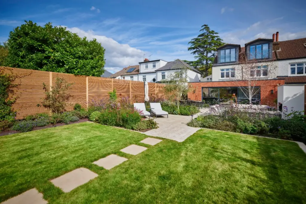 The Fire Terrace with a contemporary outdoor fireplace, modern sofas, herringbone paving and slatted timber fencing.