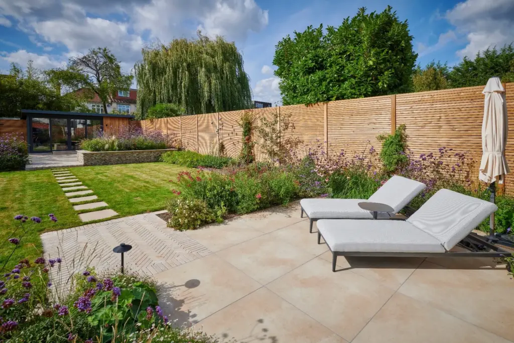 Sunbathing terrace with contemporary paving, lush planting and an open lawn.