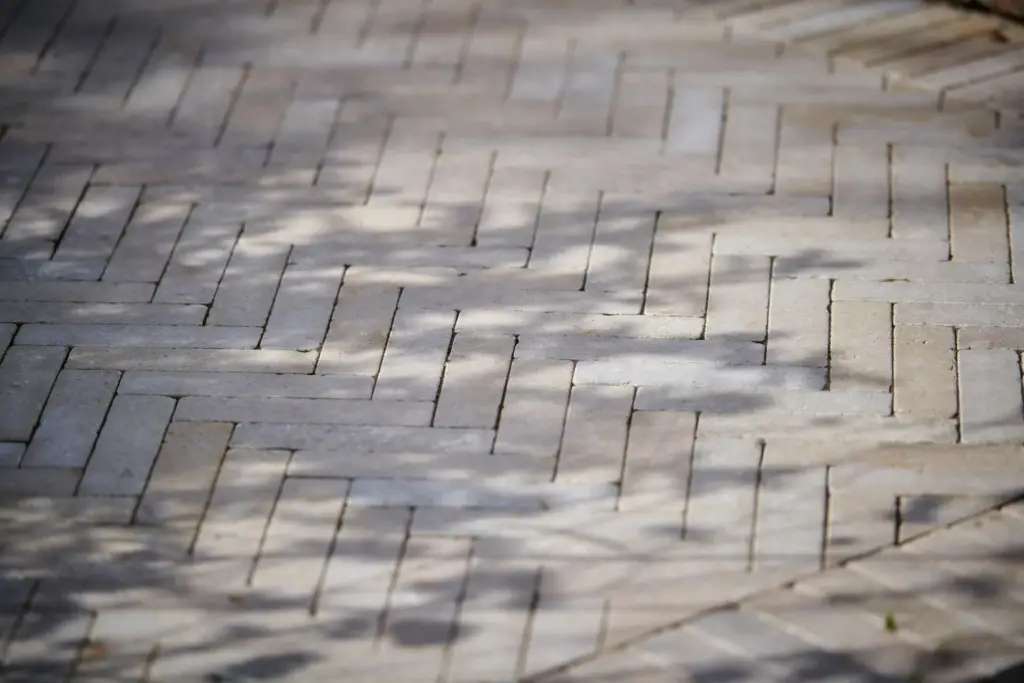 Close-up of light stone paving laid in a herringbone pattern with dappled tree shadows.