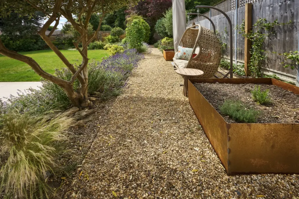 Corten steel raised beds and a hanging chair along the gravel path of the kitchen garden