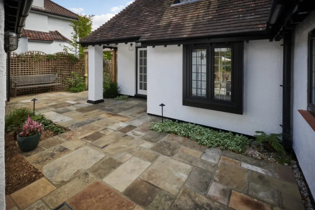 Yorkstone terrace turning the corner of the house with a planted bed and bench